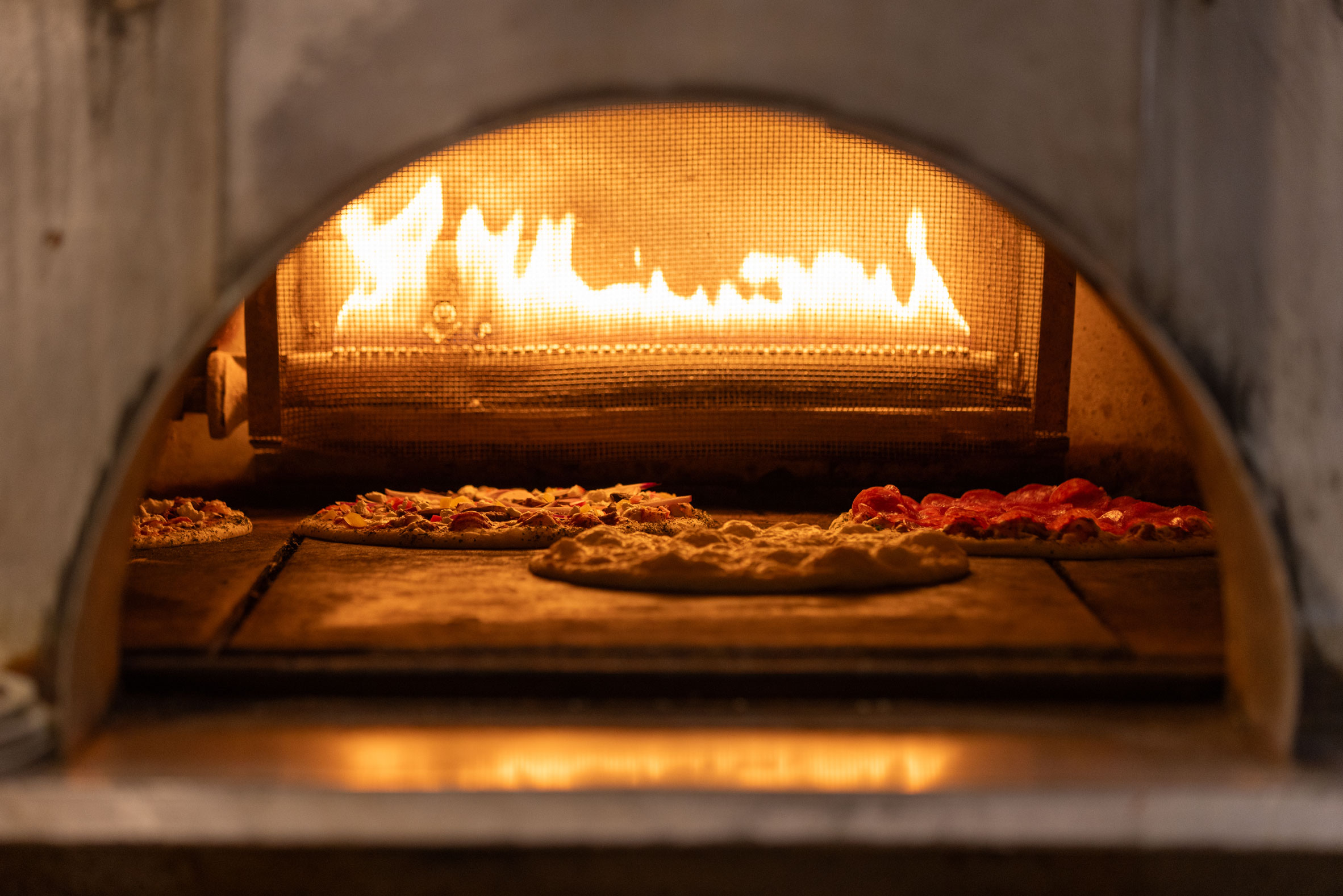 stone hearth oven fired pizza cooking with flames in the background